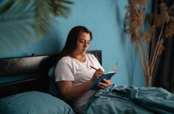 Cute,Young,Woman,Writes,A,Diary,While,Lying,In,Bed